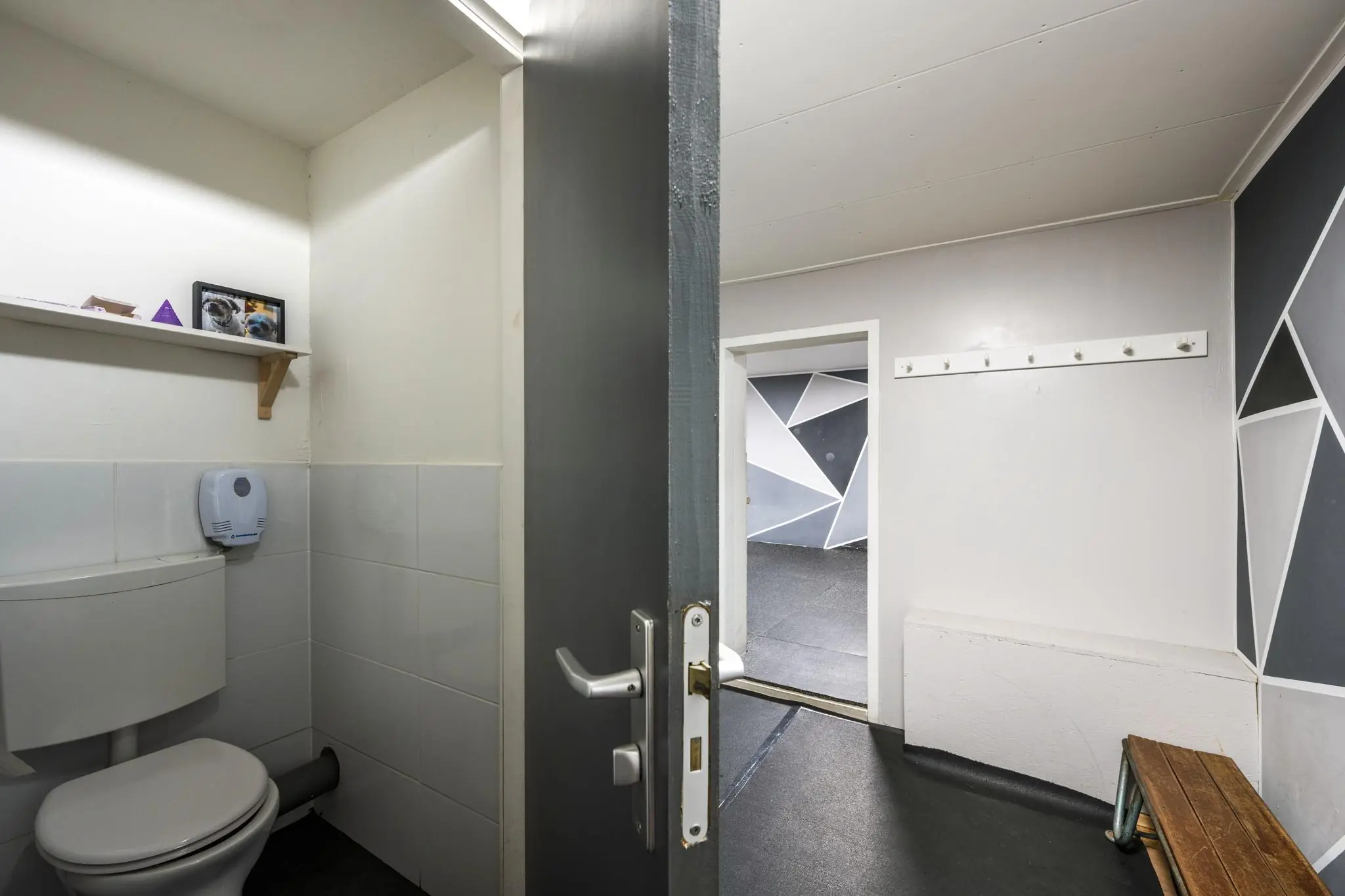 Kleine toiletruimte met open deur naar een kleedkamer in de Albert Cuypstraat, met geometrisch beschilderde muren.